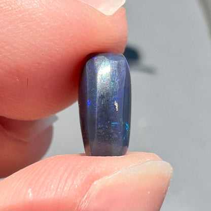 A loose Lightning Ridge black opal stone that shines colors of green, blue, and purple.