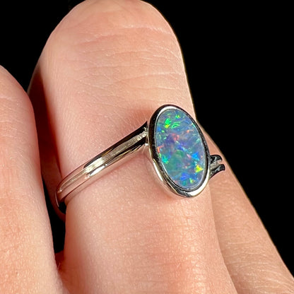 A sterling silver ring bezel-set with an oval shaped black opal doublet.  The opal has red and blue fire.