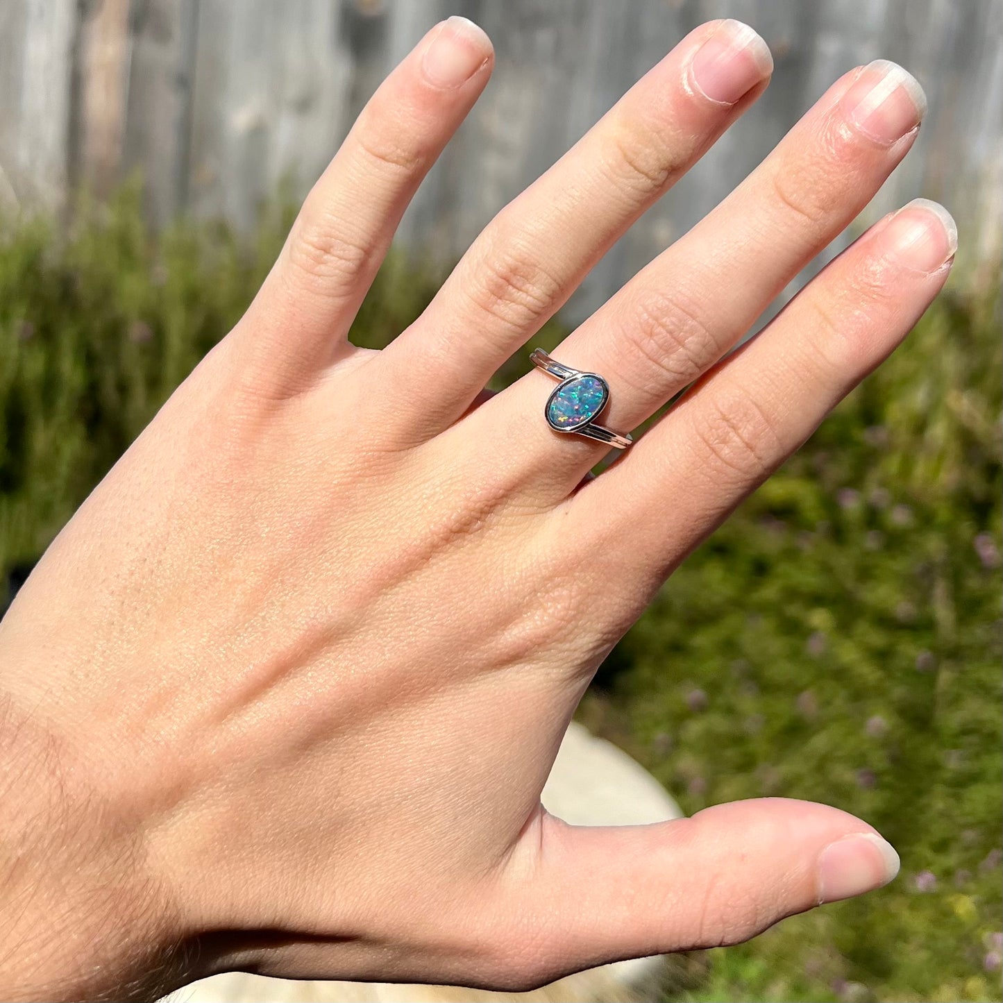 A sterling silver ring bezel-set with an oval shaped black opal doublet.  The opal has red and blue fire.