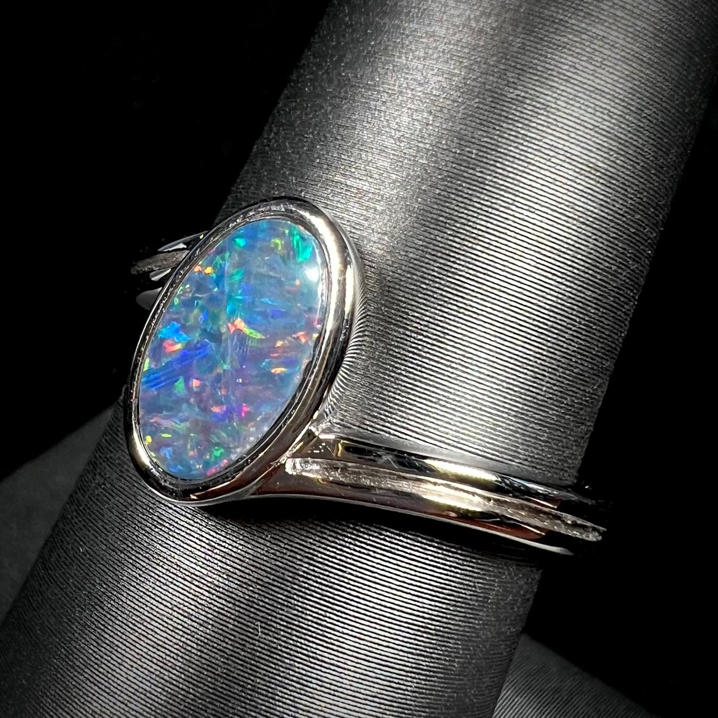 A sterling silver ring bezel-set with an oval shaped black opal doublet.  The opal has red and blue fire.