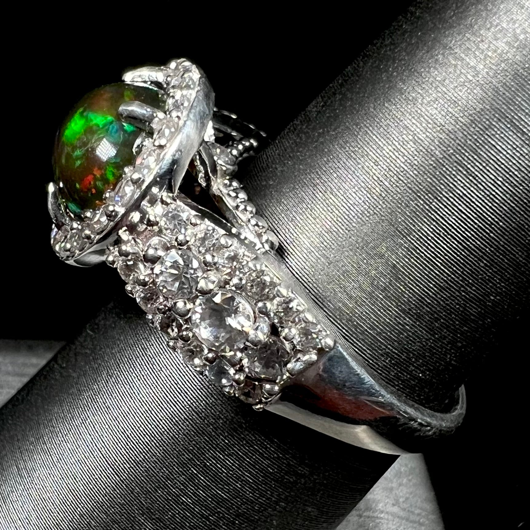 A CZ-accented sterling silver halo ring mounted with a smoked Ethiopian fire opal.  The opal plays green, red, and blue colors.