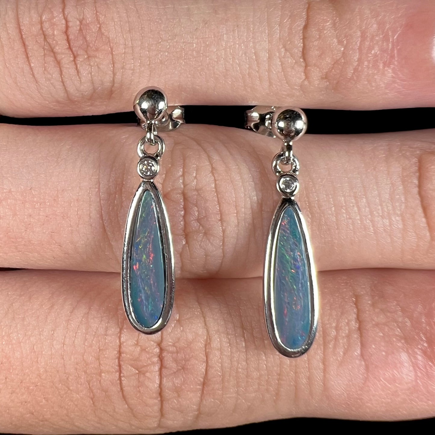 A pair of sterling silver, pear shaped opal doublet dangle earrings.  The opals have a gray body tone with red fire.