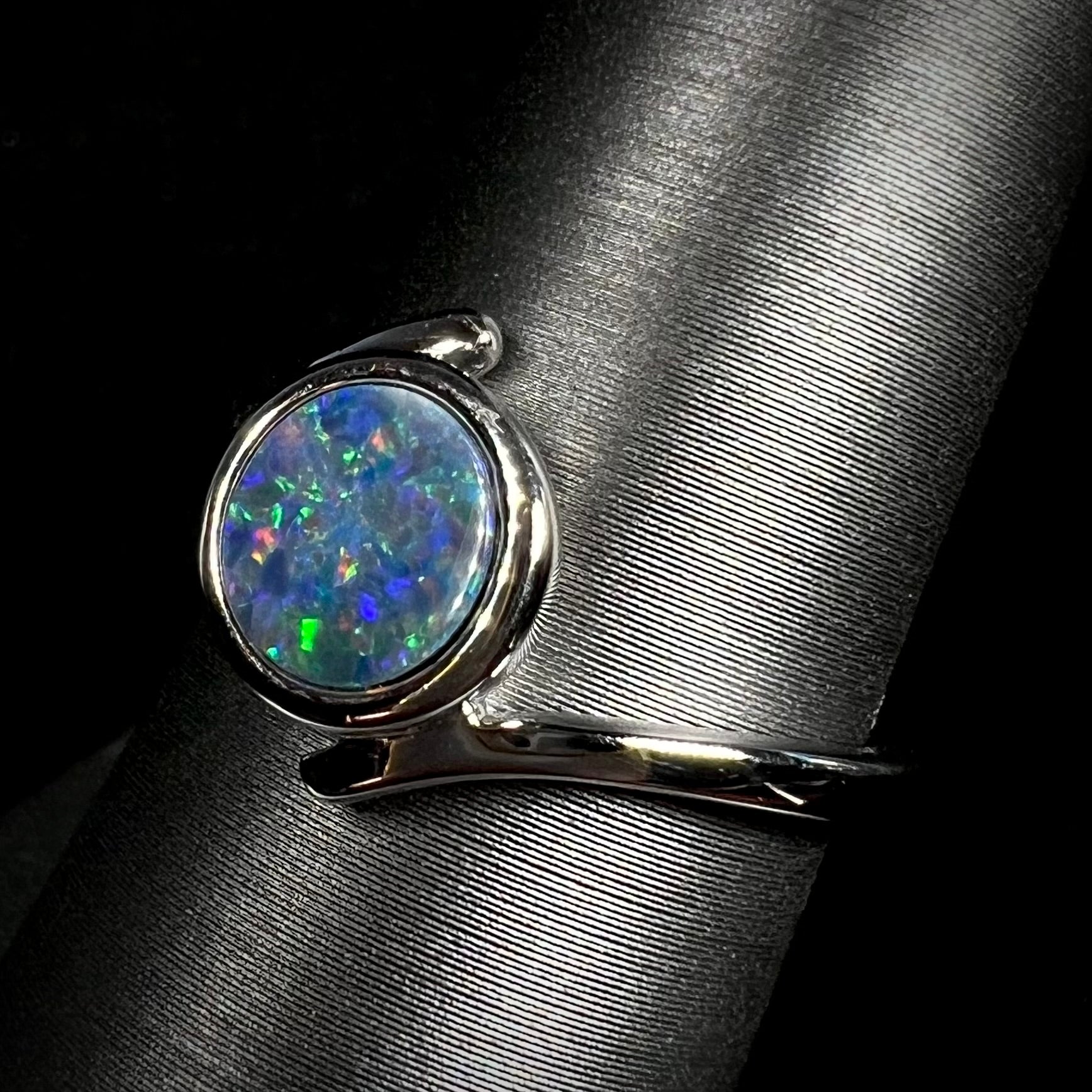 A sterling silver bypass ring bezel-set with a round cut black opal doublet.