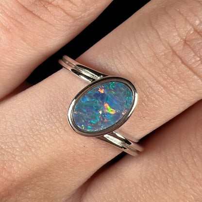 A sterling silver ring bezel-set with an oval shaped black opal doublet.  The opal has red and blue fire.