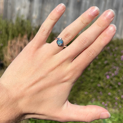 A sterling silver bypass ring bezel-set with a round cut black opal doublet.