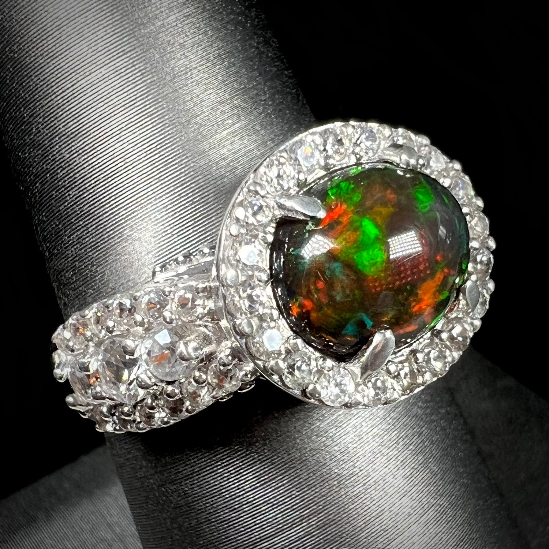 A CZ-accented sterling silver halo ring mounted with a smoked Ethiopian fire opal.  The opal plays green, red, and blue colors.