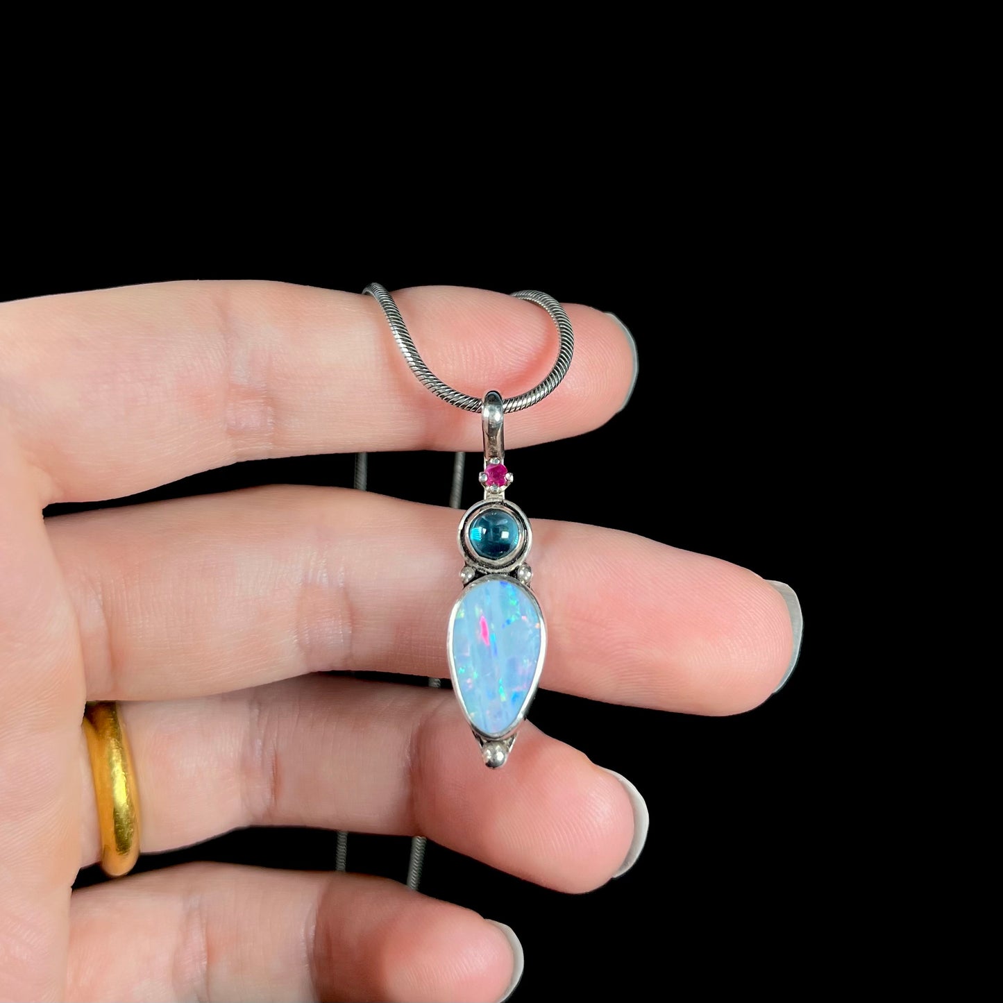 A sterling silver necklace shaped like a child, mounted with an opal doublet, a ruby, and a blue piece of glass.