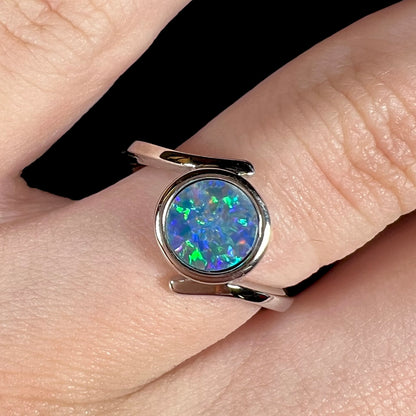 A sterling silver bypass ring bezel-set with a round cut black opal doublet.