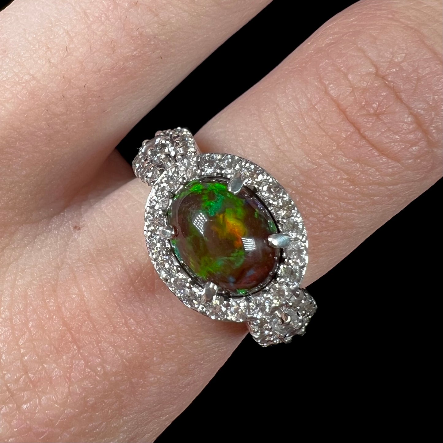 A CZ-accented sterling silver halo ring mounted with a smoked Ethiopian fire opal.  The opal plays green, red, and blue colors.