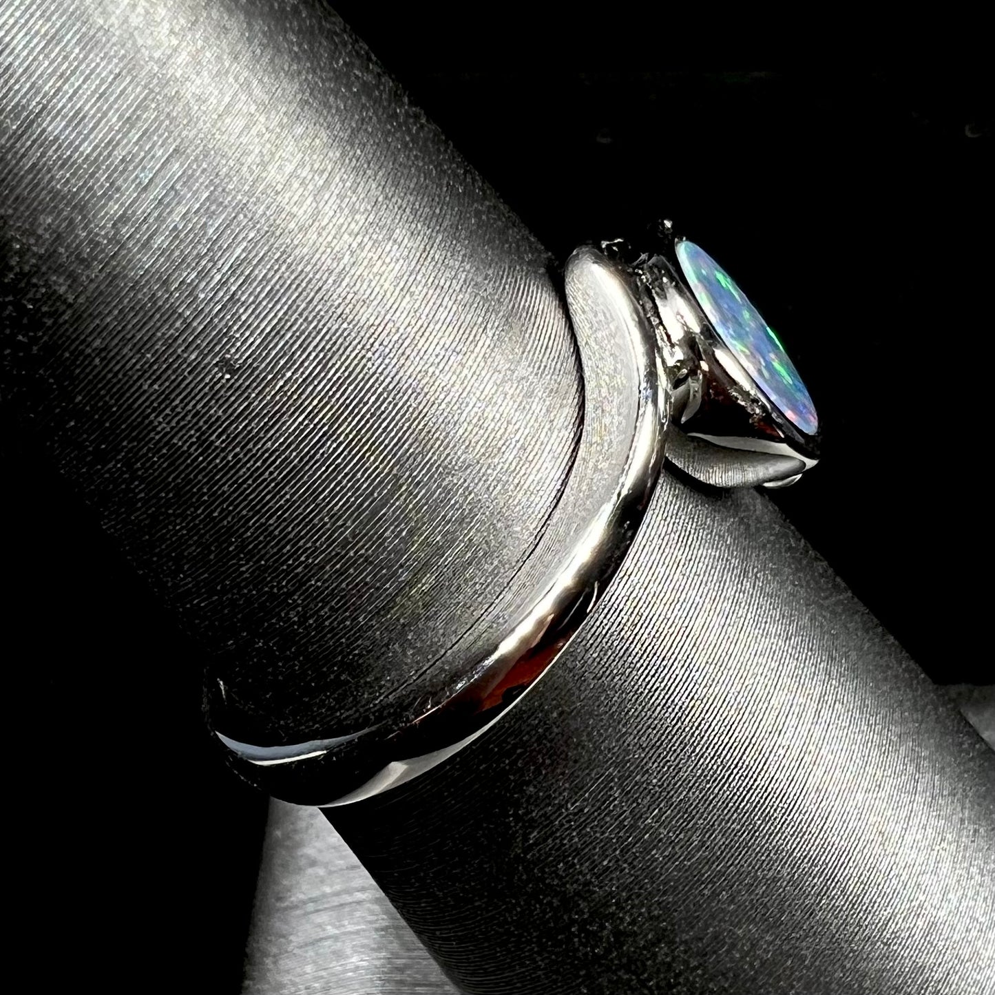 A sterling silver bypass ring bezel-set with a round cut black opal doublet.