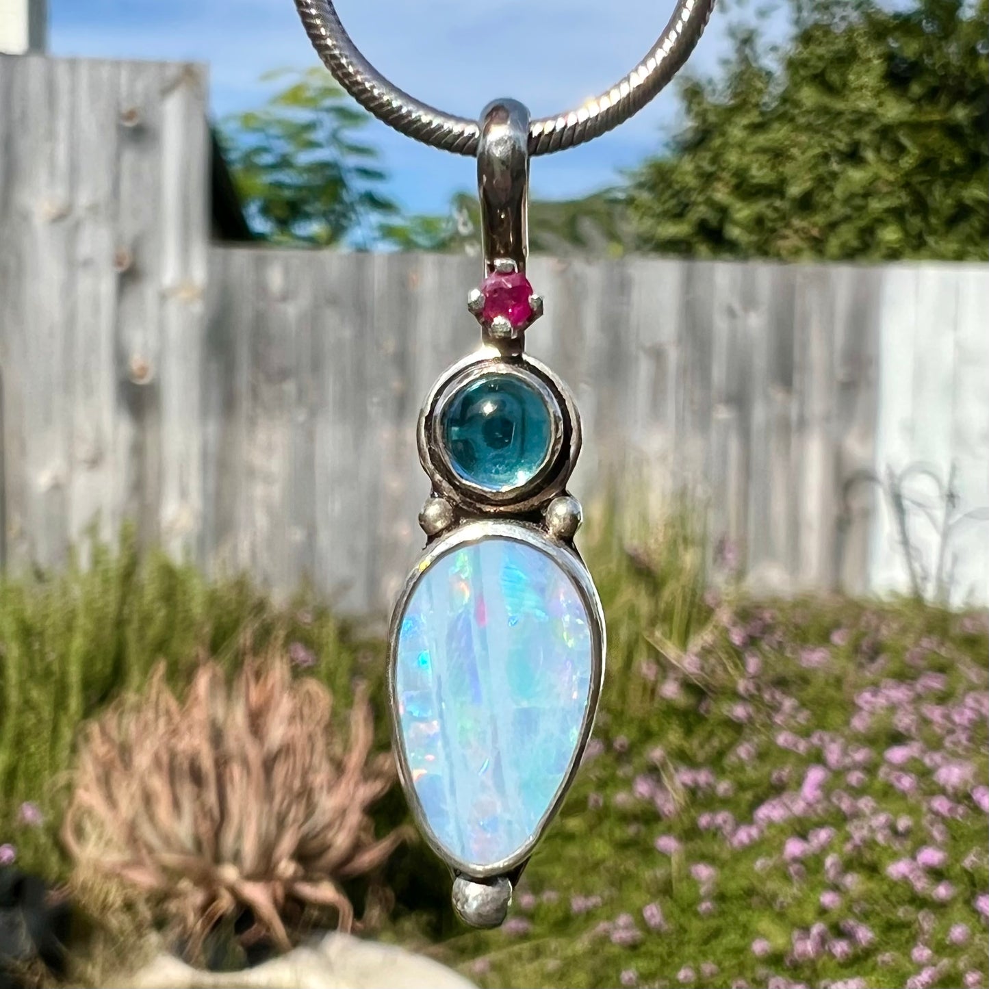 A sterling silver necklace shaped like a child, mounted with an opal doublet, a ruby, and a blue piece of glass.