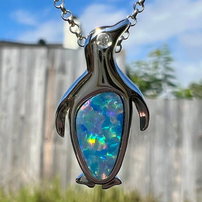 A sterling silver penguin necklace inlaid with a black opal doublet and a CZ accent in the penguin's eye.