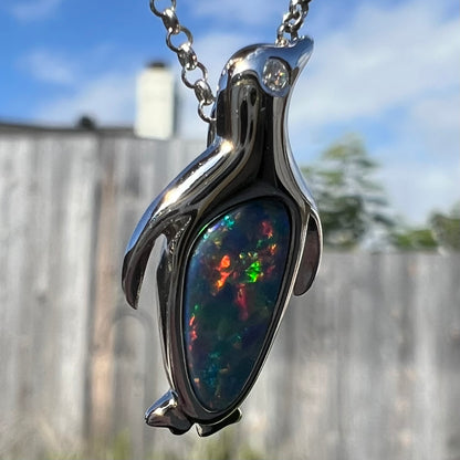 A sterling silver penguin necklace inlaid with a black opal doublet and a CZ accent in the penguin's eye.