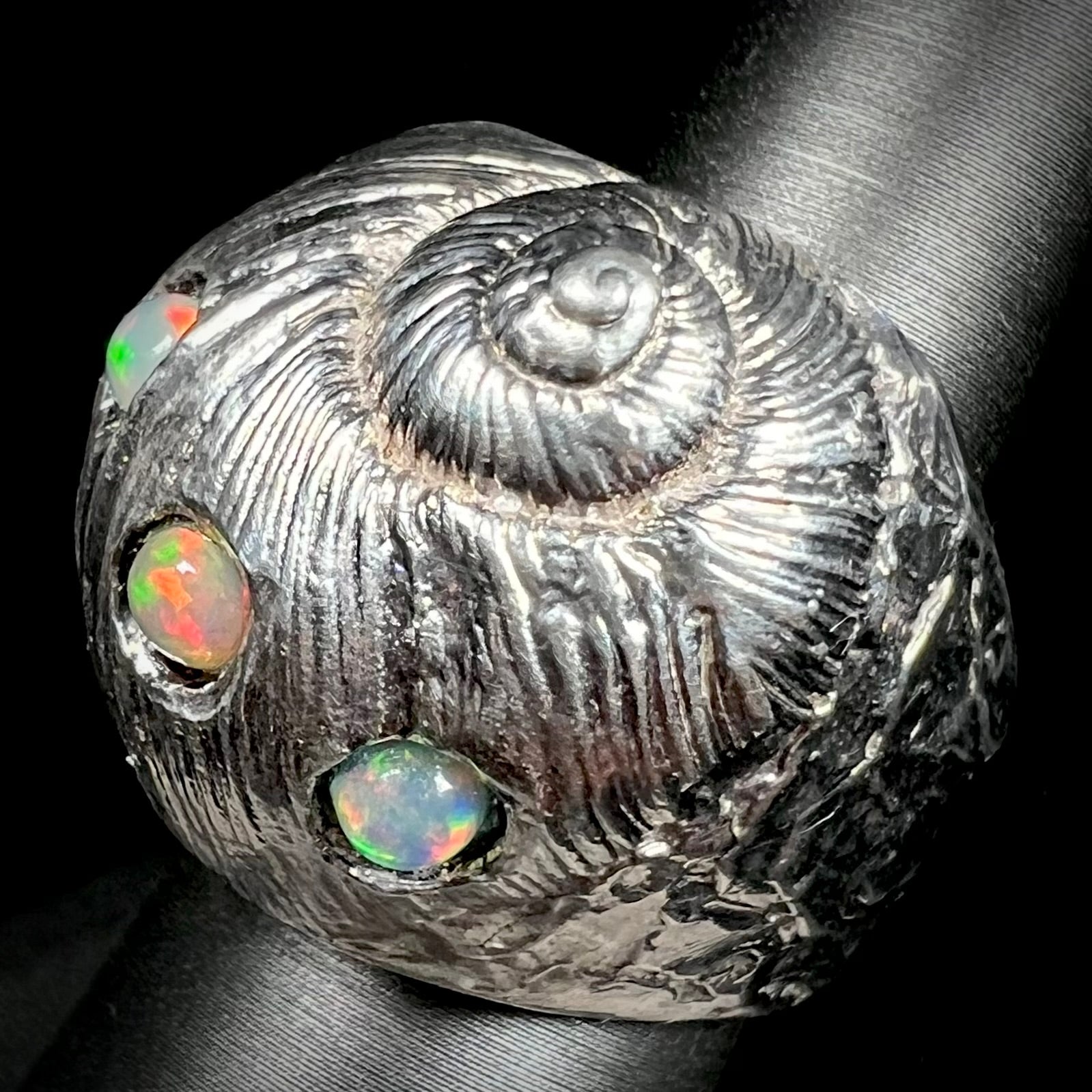 A large, three dimensional sterling silver snail seashell ring set with three round Ethiopian fire opal stones.