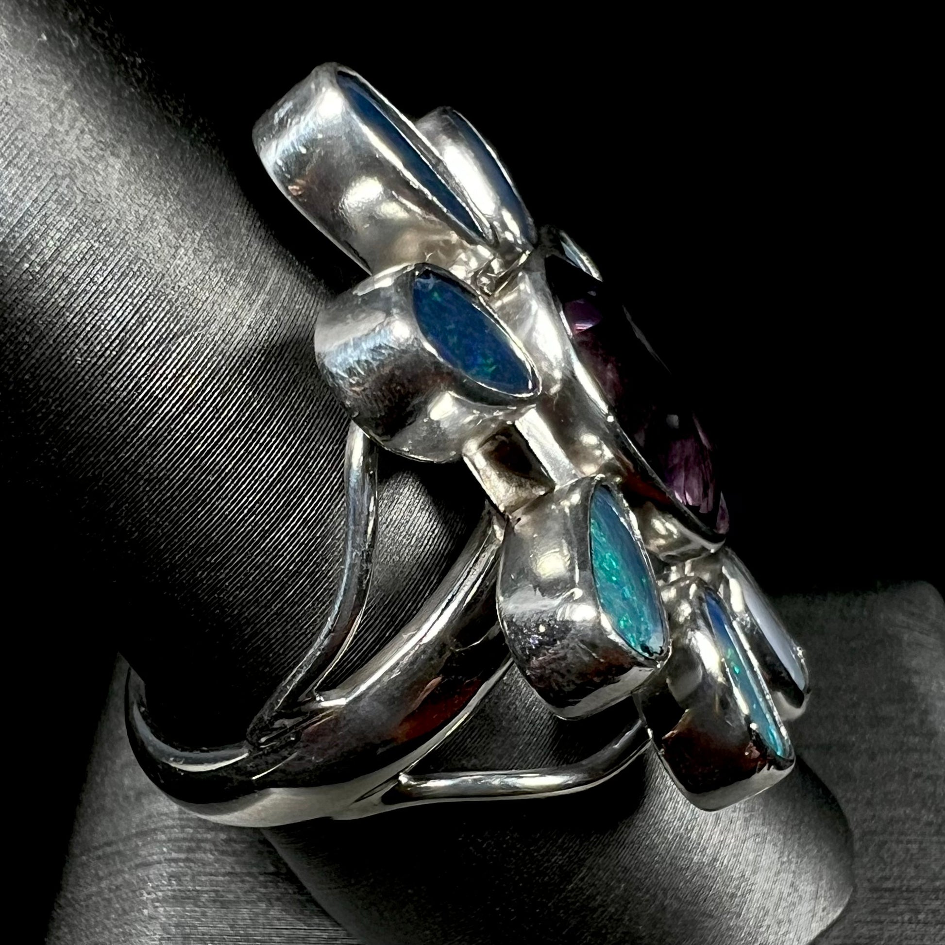 A sterling silver flower shaped ring set with an oval cut amethyst in the center and black opal doublet petals.