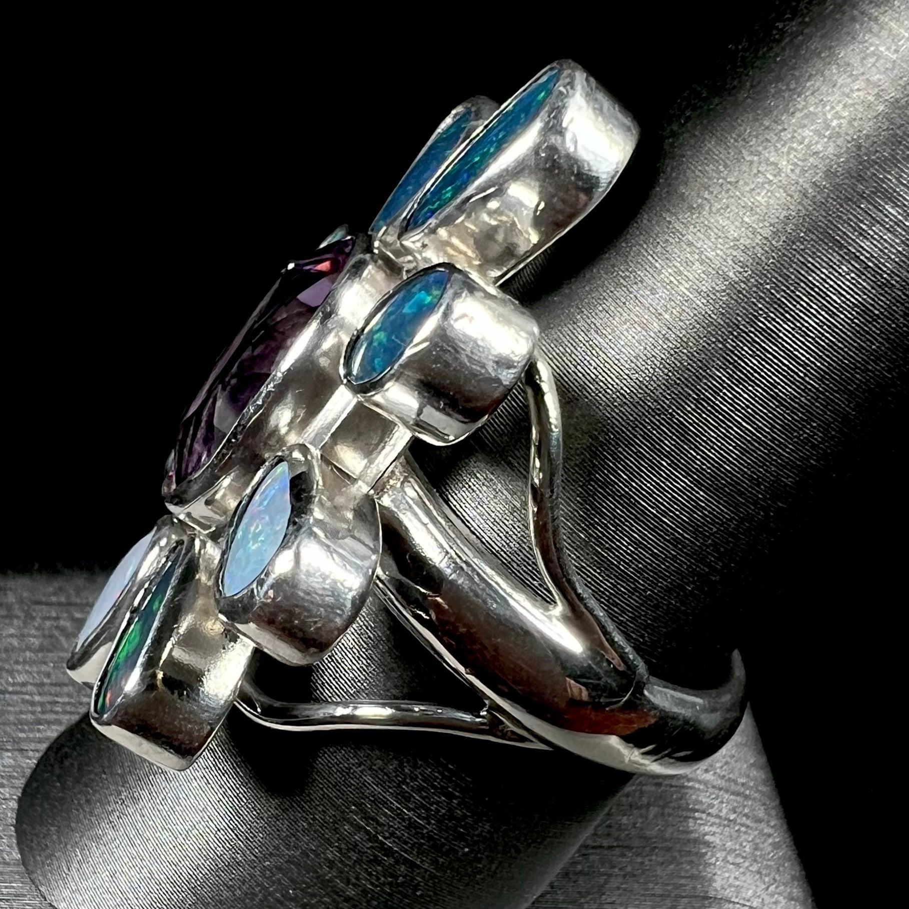 A sterling silver flower shaped ring set with an oval cut amethyst in the center and black opal doublet petals.