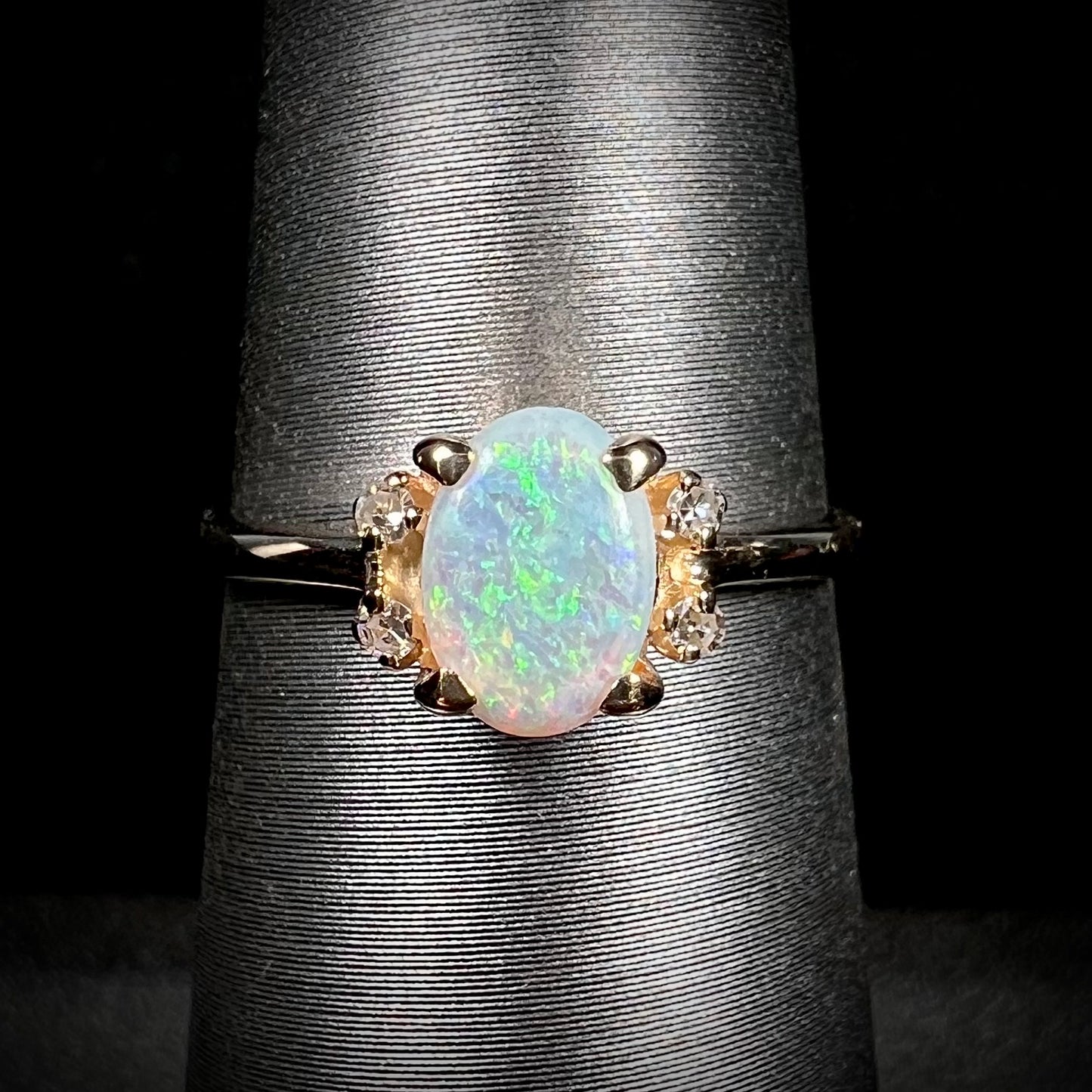 A dainty yellow gold ring set with a Coober Pedy opal with green flashfire pattern and diamond accents.