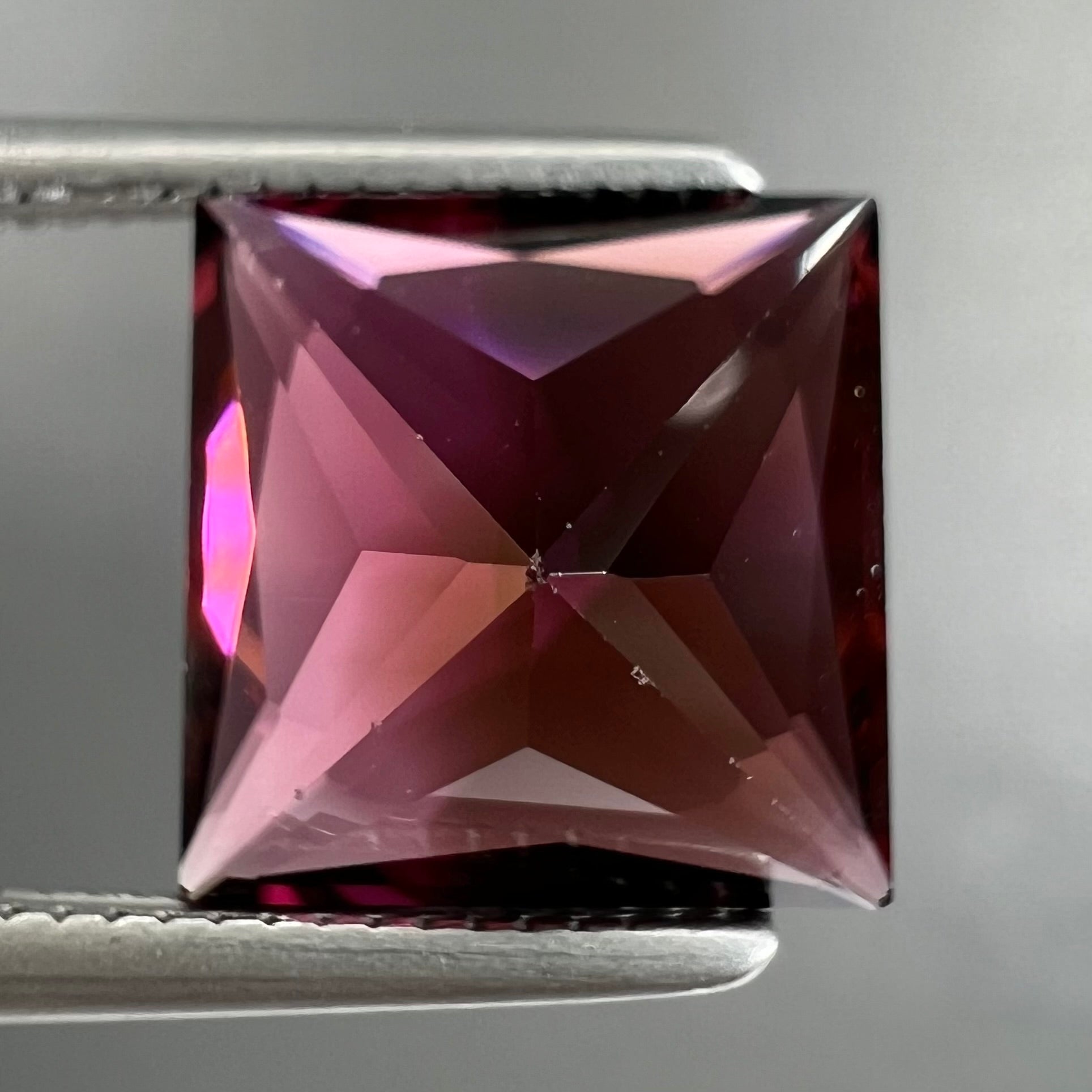 A loose, faceted princess cut tourmaline gemstone.  The stone is a burgundy purple color.