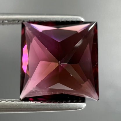 A loose, faceted princess cut tourmaline gemstone.  The stone is a burgundy purple color.