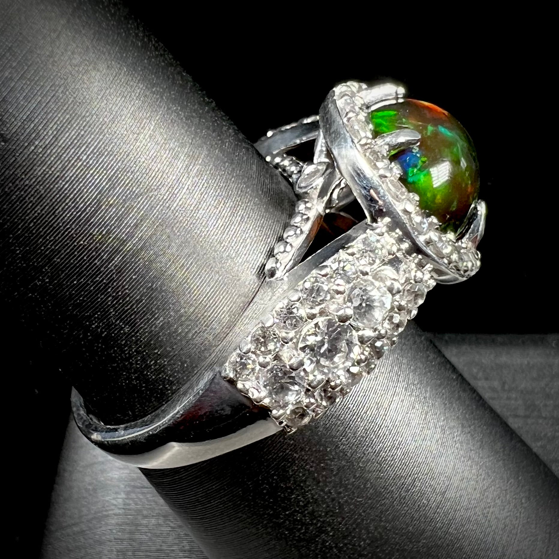 A CZ-accented sterling silver halo ring mounted with a smoked Ethiopian fire opal.  The opal plays green, red, and blue colors.