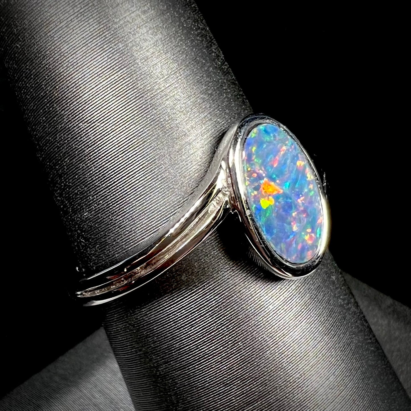 A sterling silver ring bezel-set with an oval shaped black opal doublet.  The opal has red and blue fire.