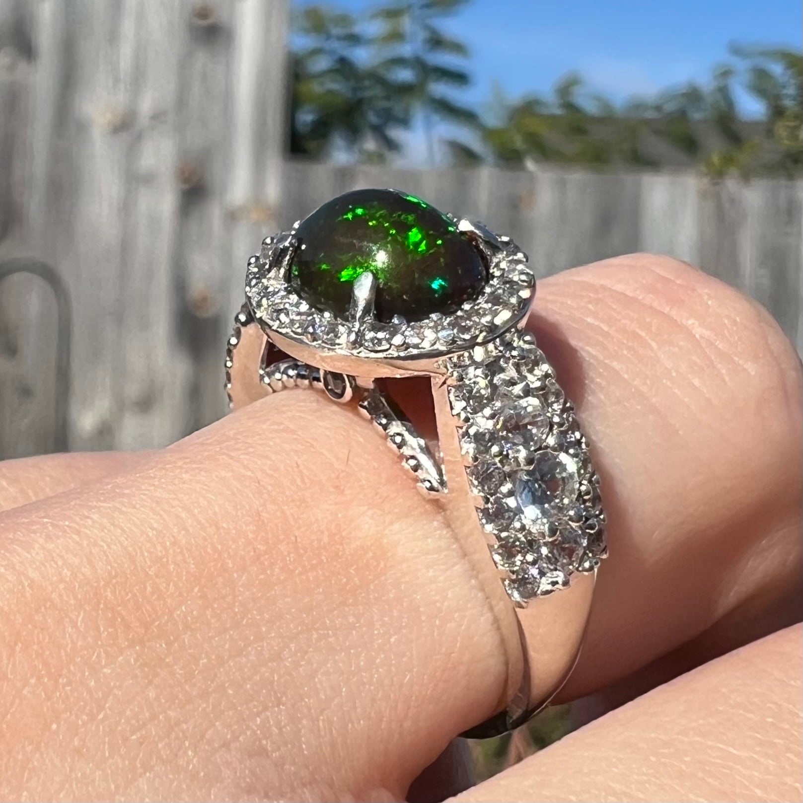 A CZ-accented sterling silver halo ring mounted with a smoked Ethiopian fire opal.  The opal plays green, red, and blue colors.