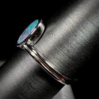 A sterling silver ring bezel-set with an oval shaped black opal doublet.  The opal has red and blue fire.