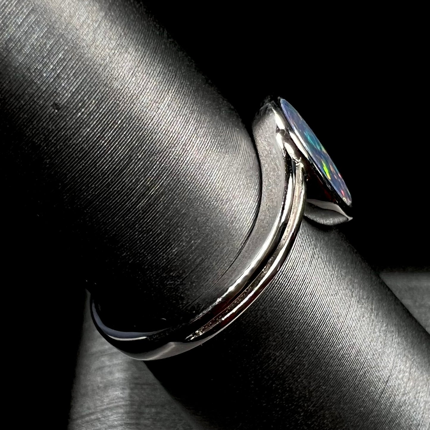 A sterling silver ring bezel-set with an oval shaped black opal doublet.  The opal has red and blue fire.