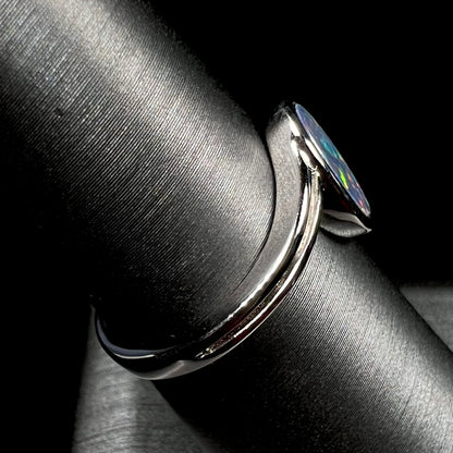 A sterling silver ring bezel-set with an oval shaped black opal doublet.  The opal has red and blue fire.