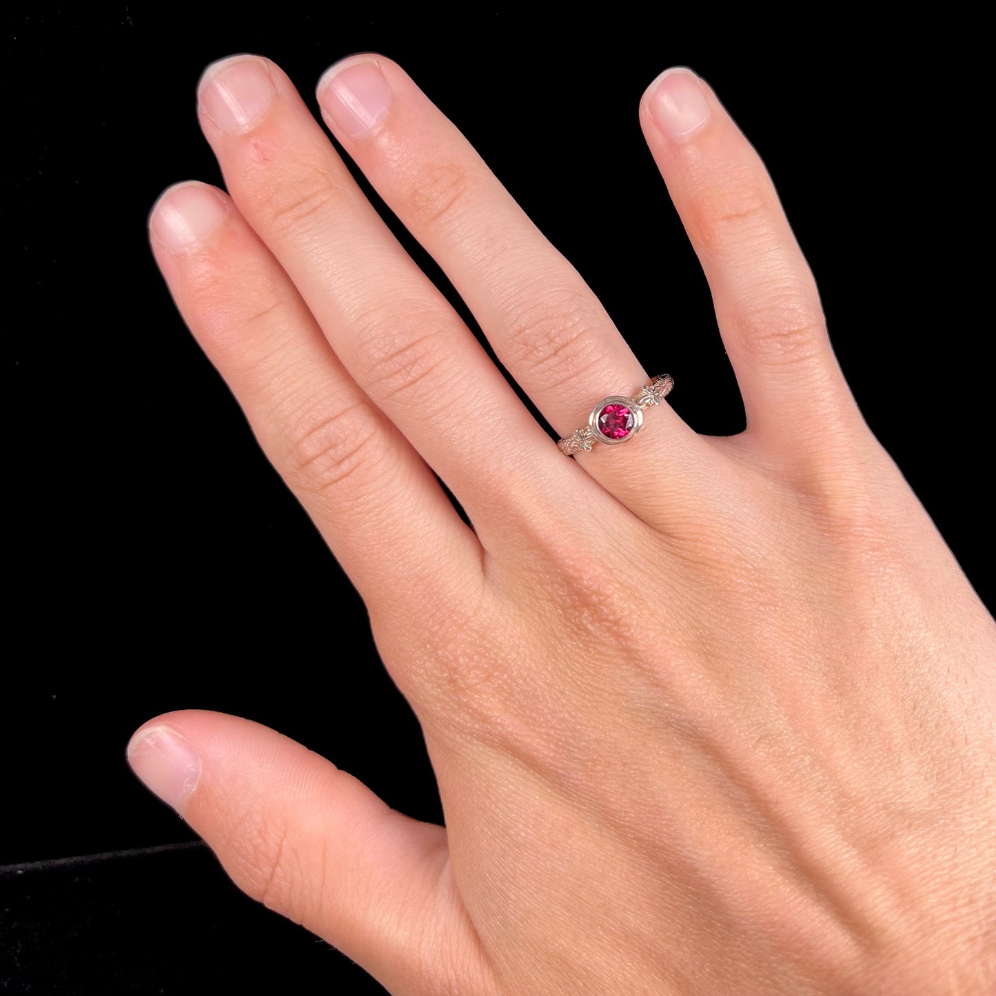 A ladies' sterling silver purple rhodonite garnet solitaire ring.  The shank has an etched floral leaf design.