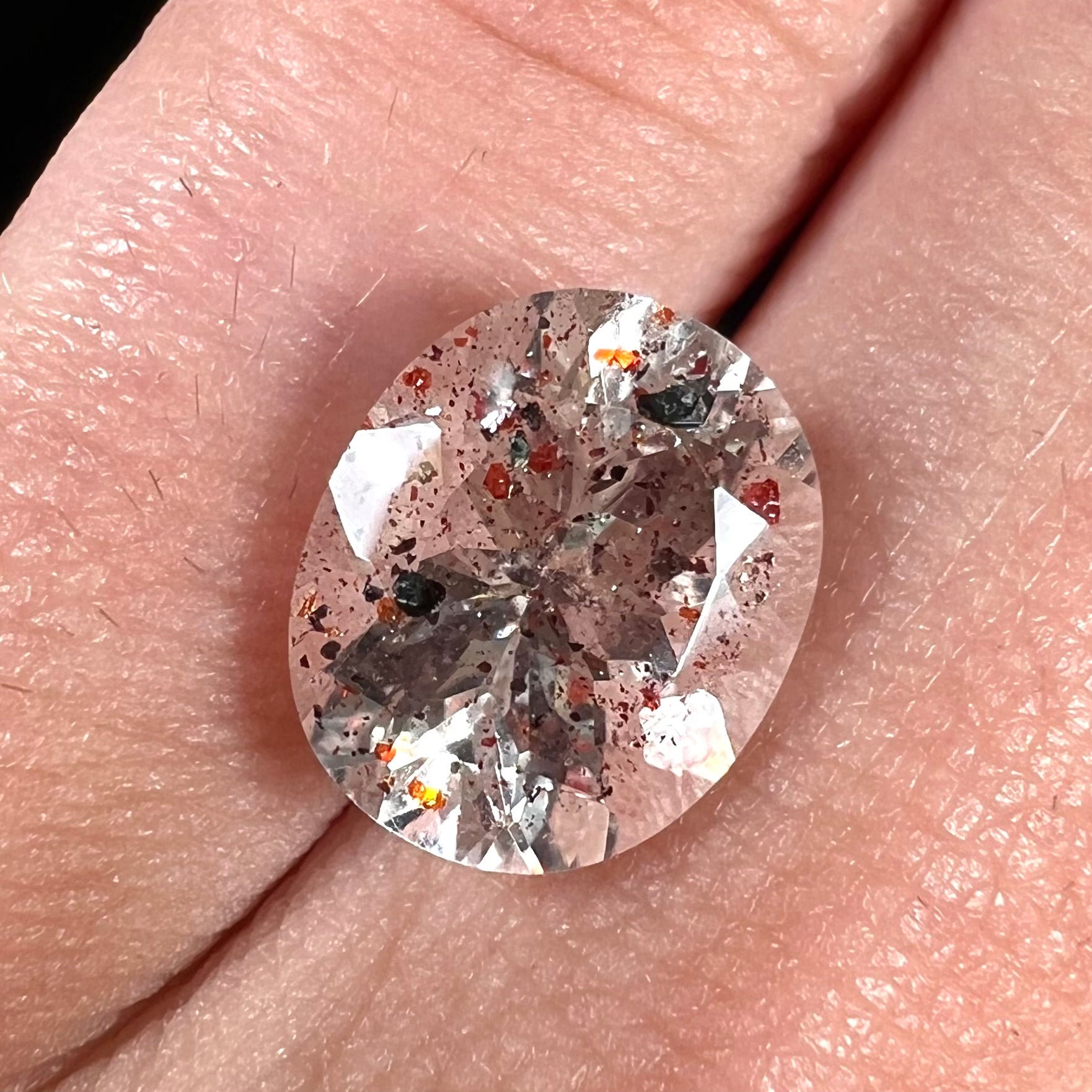 A loose, faceted oval cut lepidocrocite quartz stone.  The stone has red and black inclusions.