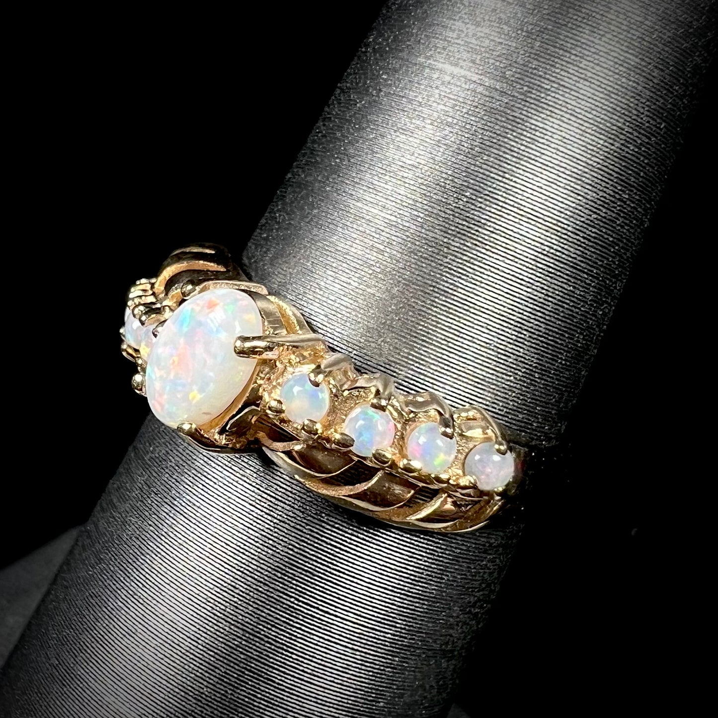 A yellow gold ring featuring two crossing, alternating lines of round cut synthetic opals.  In the middle is a larger oval cut synthetic opal.