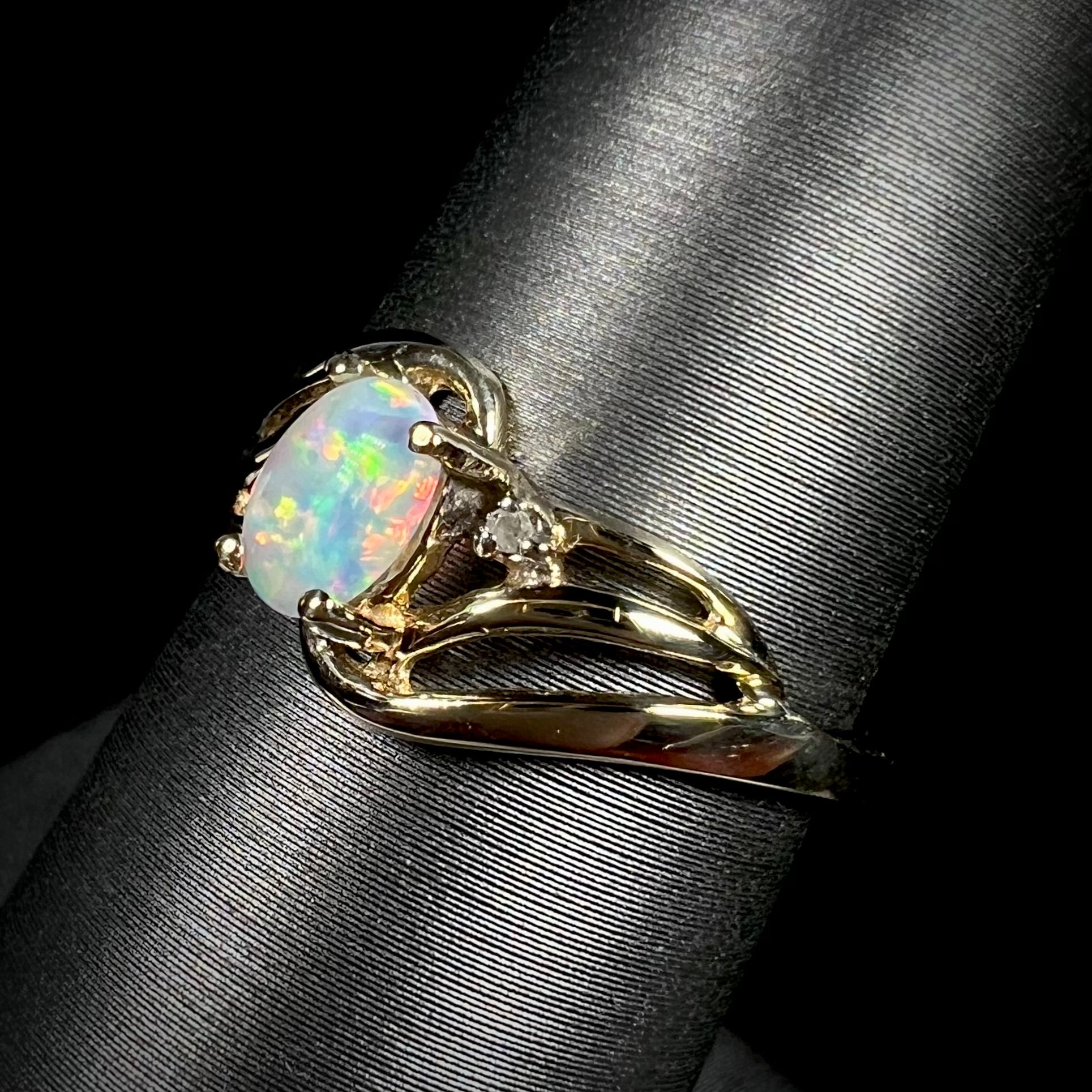 A yellow gold ring mounted with two diamond accents and an oval cut lab created opal.  The opal has bright red colors.