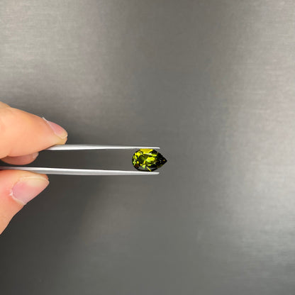 A loose, pear shaped green tourmaline gemstone.  The color is dark green with a yellow secondary hue.