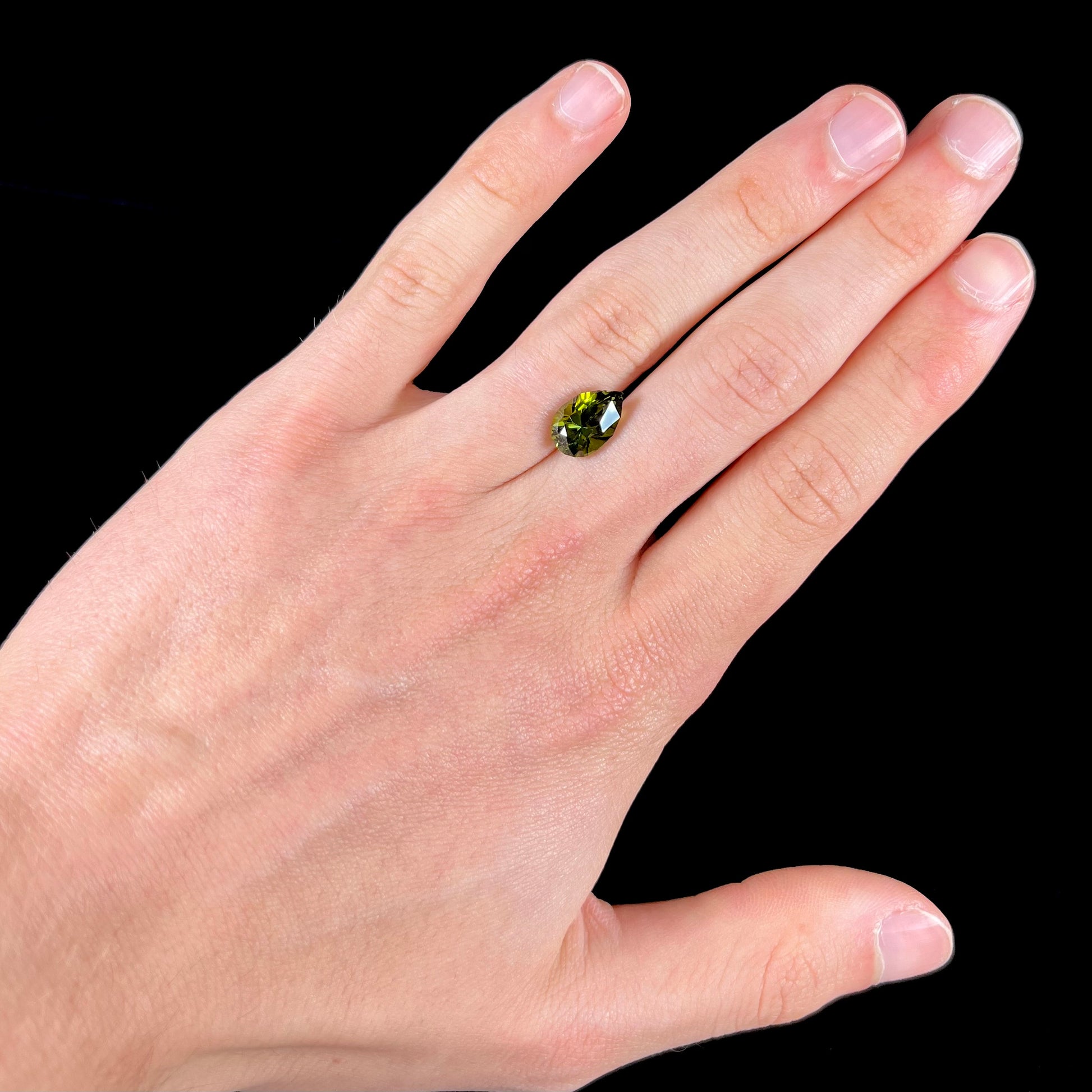 A loose, pear shaped green tourmaline gemstone.  The color is dark green with a yellow secondary hue.