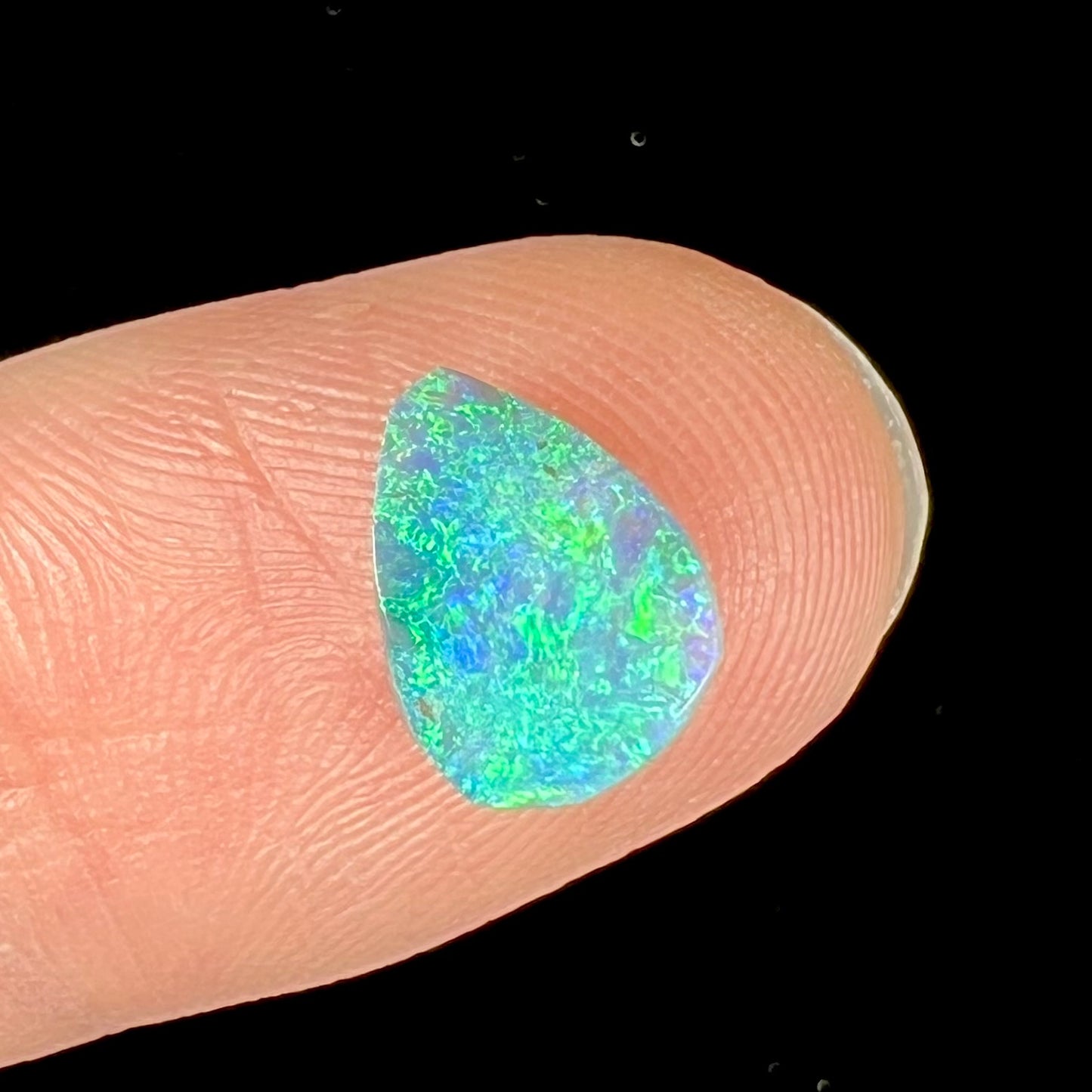 A loose, pear shaped black opal from LIghtning Ridge, Australia.  The opal shines blue and green colors.