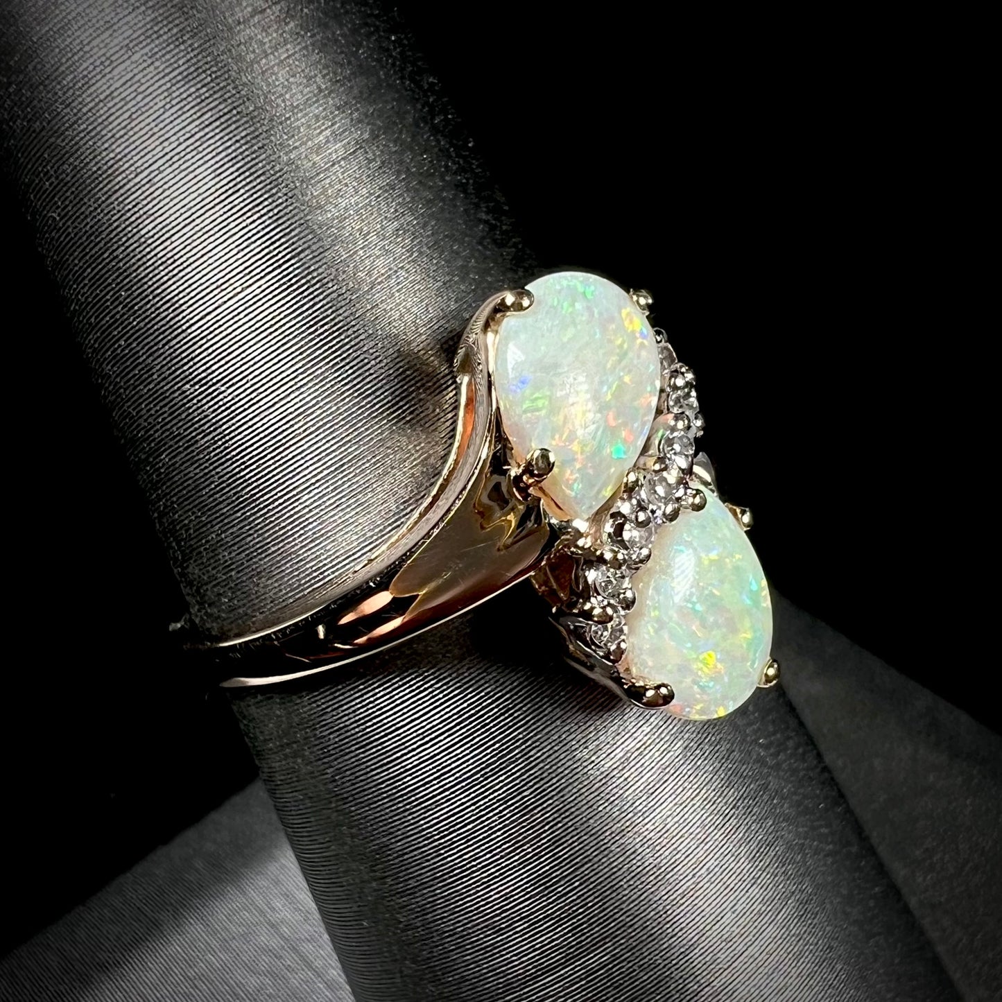 A yellow gold ring mounted with two pear shaped opals and diamond accents  The stones form an infinity shaped design.