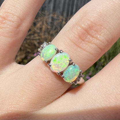 A ladies' white gold ring prong-set with three natural white opals and diamond accents.  The opals play a green color.