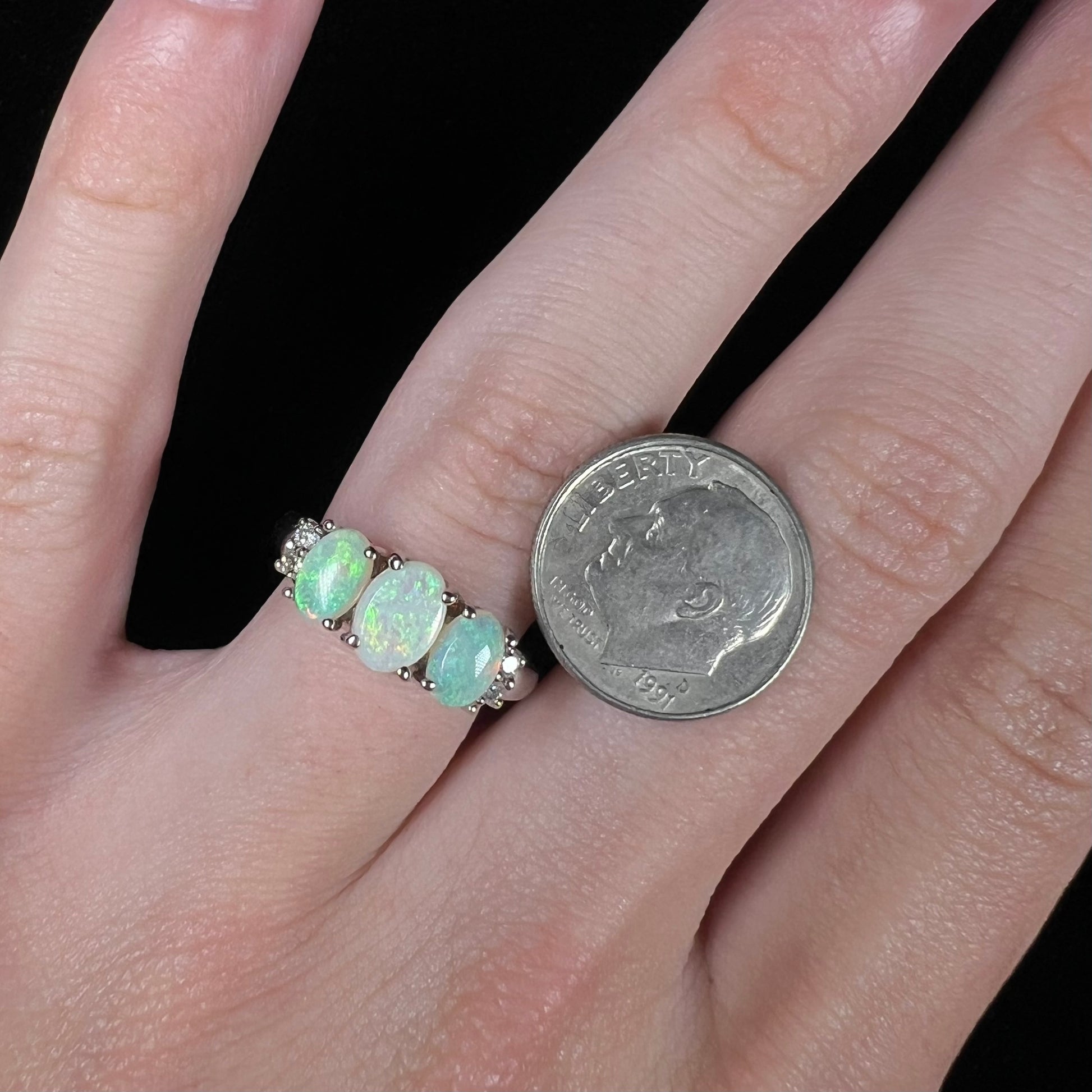 A ladies' white gold ring prong-set with three natural white opals and diamond accents.  The opals play a green color.