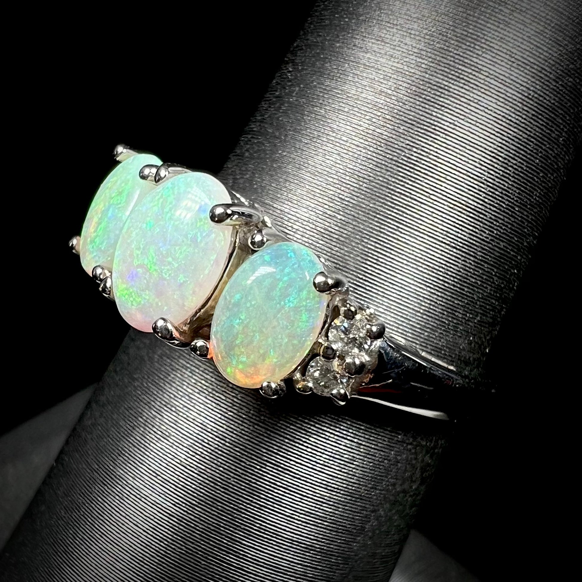 A ladies' white gold ring prong-set with three natural white opals and diamond accents.  The opals play a green color.