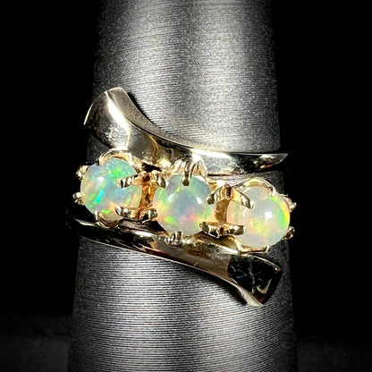 A yellow gold bypass shank ring mounted with three round cabochon cut Ethiopian fire opals.