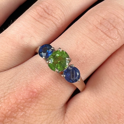 A ladies' white gold three stone ring set with two round blue sapphires and an oval cut green tsavorite garnet.