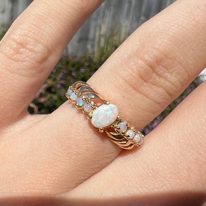 A yellow gold ring featuring two crossing, alternating lines of round cut synthetic opals.  In the middle is a larger oval cut synthetic opal.