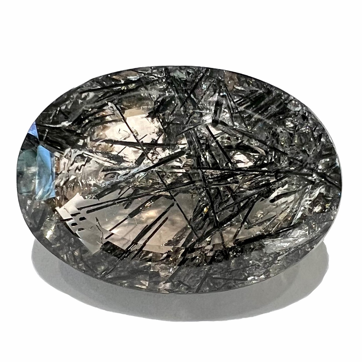 A loose, faceted oval cut smoky quartz stone with black tourmaline crystal inclusions.  The gem weighs 35.68 carats.
