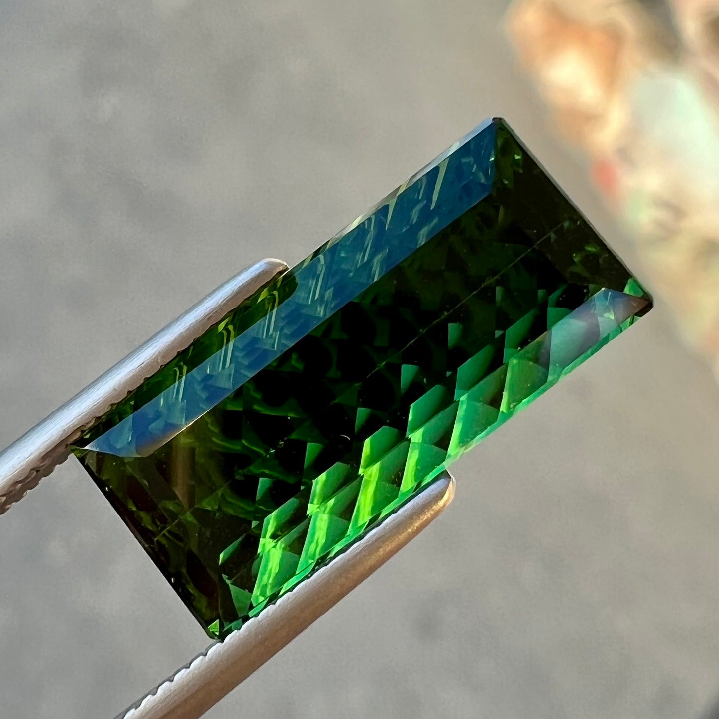 A loose, rectangular laser cut green tourmaline gemstone.