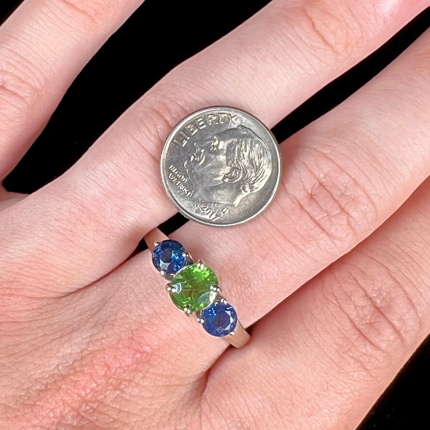 A ladies' white gold three stone ring set with two round blue sapphires and an oval cut green tsavorite garnet.