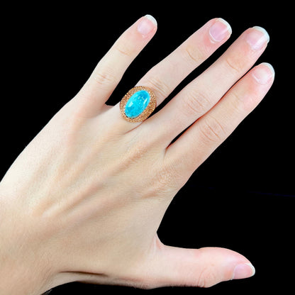 A yellow gold filigree style ring mounted with an oval Pilot Mountain turquoise stone.