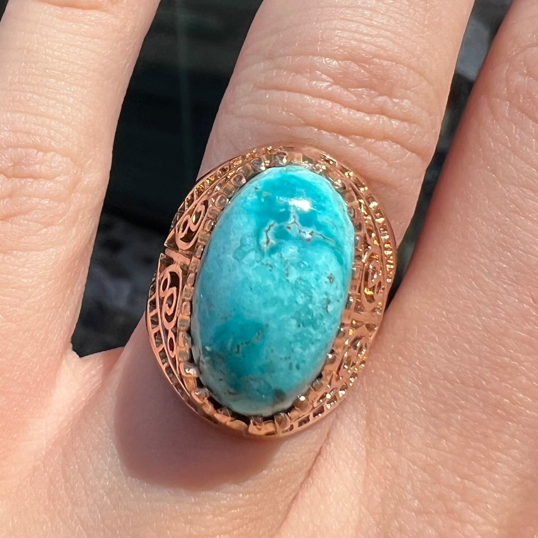 A yellow gold filigree style ring mounted with an oval Pilot Mountain turquoise stone.