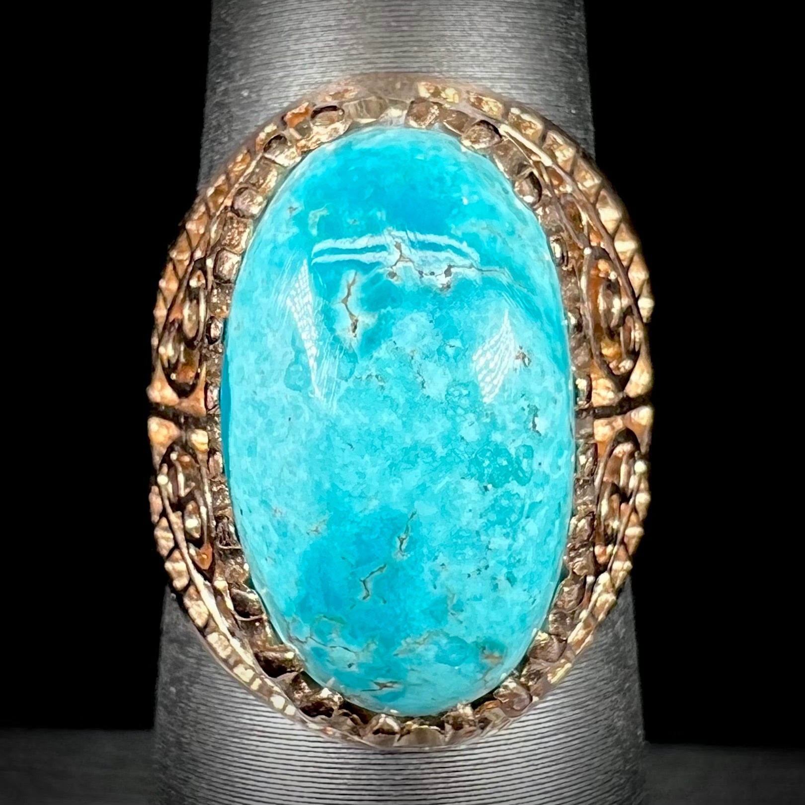 A yellow gold filigree style ring mounted with an oval Pilot Mountain turquoise stone.