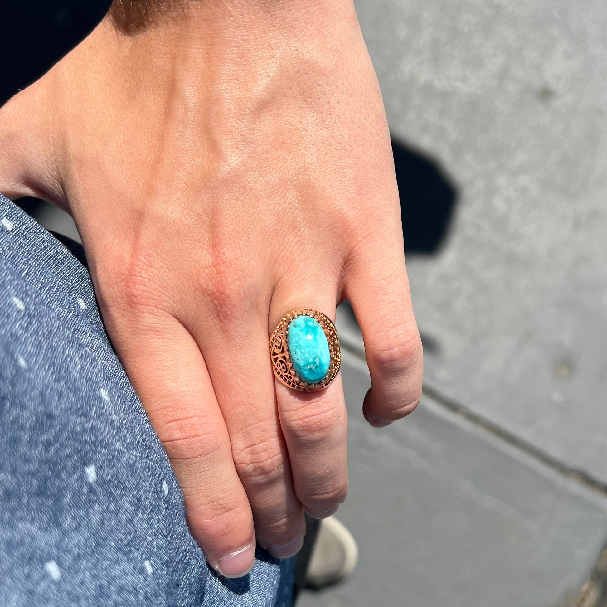 A yellow gold filigree style ring mounted with an oval Pilot Mountain turquoise stone.